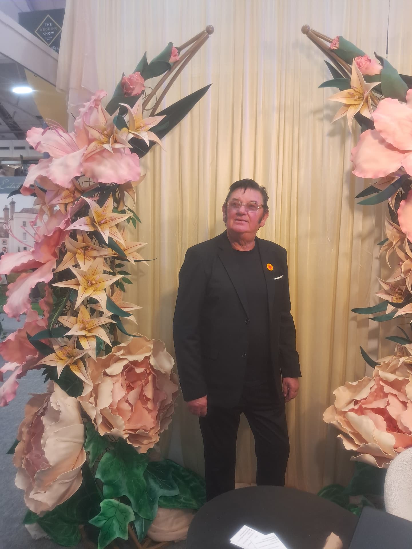 Greg Traynor, celebrant and solemniser, standing between large floral arrangements at a wedding showcase
